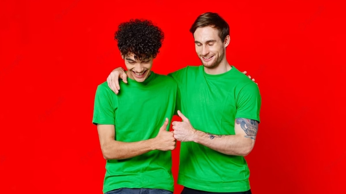 Two gay men wearing matching green tees, standing with hands on each other shoulder in a red background.