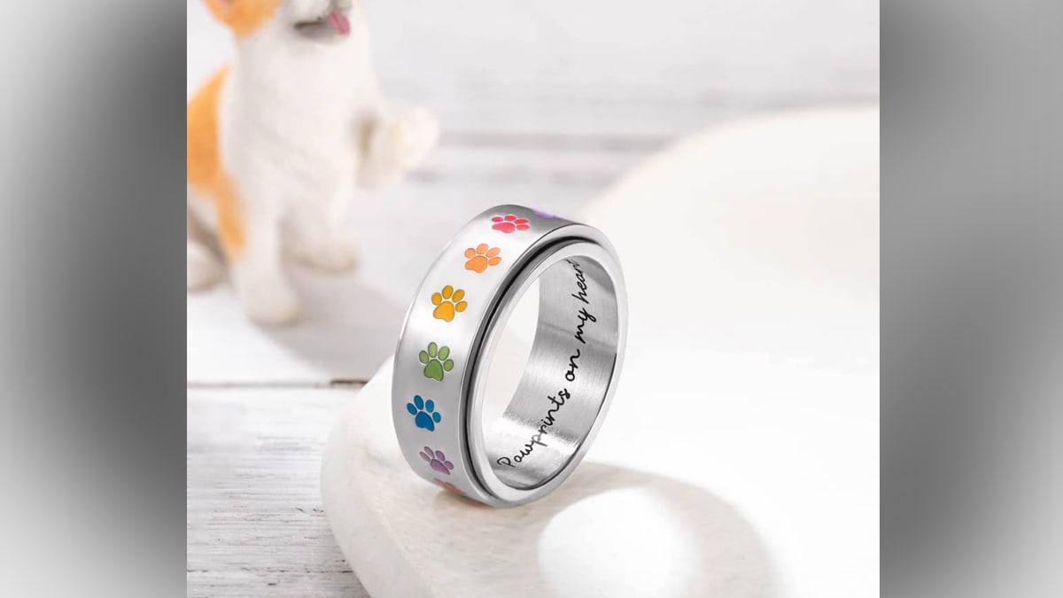 A rainbow paw print ring with a quote engraved Pawprints on my heart placed on a white table.