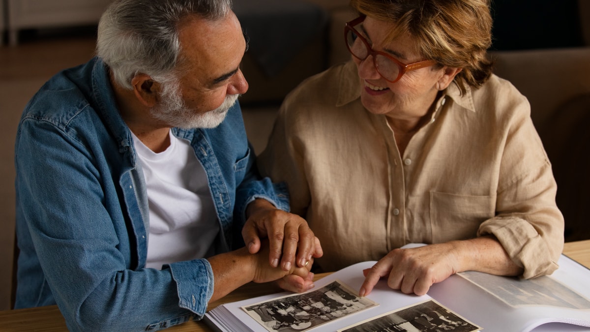 An old age couple looking at each other smiling while going through the old photographs