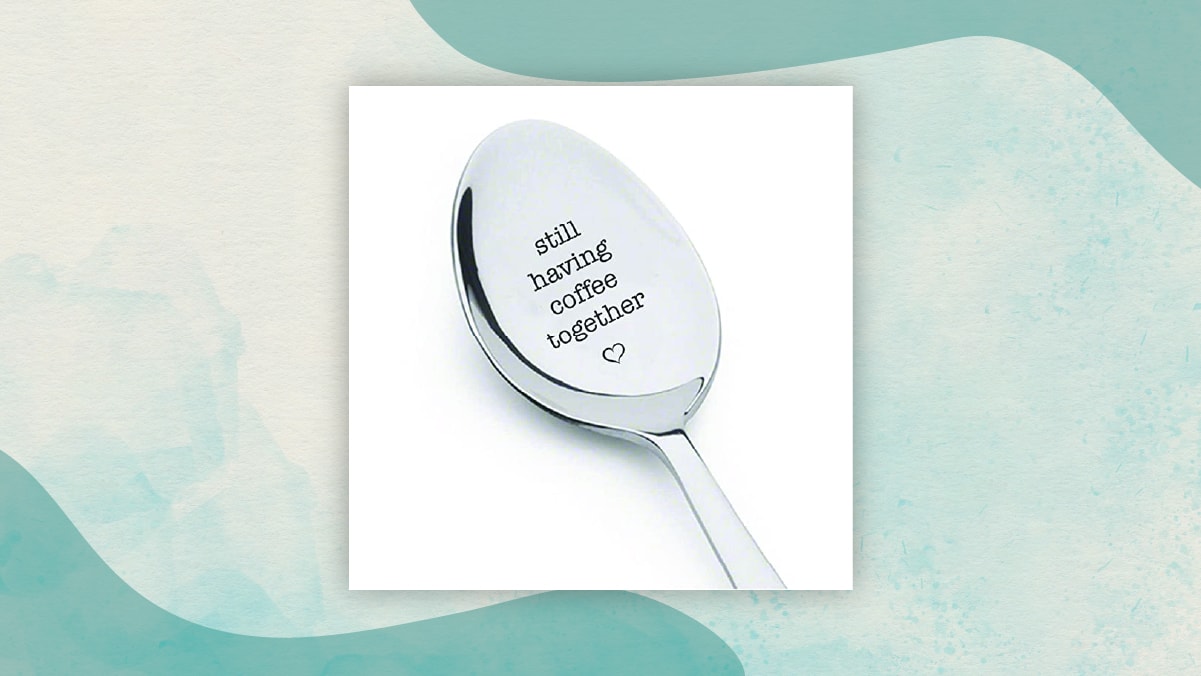 A spoon with "still having coffee together" written on it and a small heart shape below it in a white background.