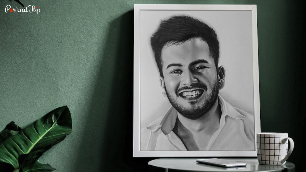 A handmade charcoal painting of a man smiling placed on a table created by PortraitFlip.
