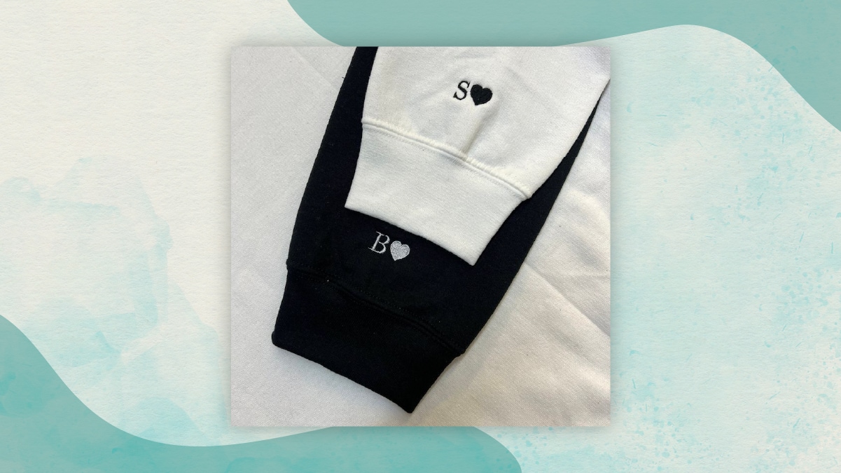 A black and a white sleeve with initials B and S embroidered with hearts on the cuffs kept on a white bedsheet as best gifts for long distance relationships. 