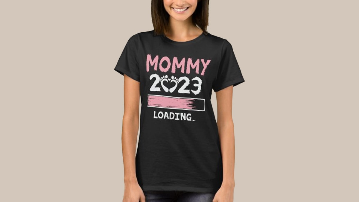 A women standing in a black top in a cream colored background with "Mommy 2023" written on it as mother's day gift ideas. 