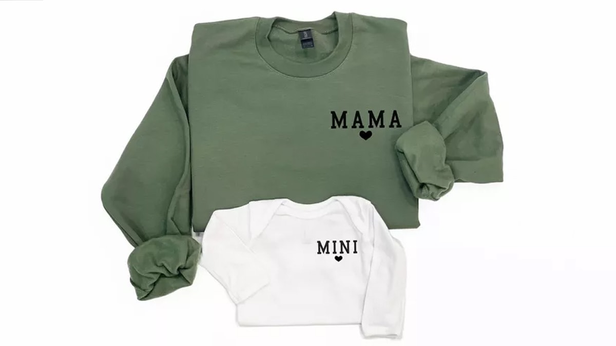 Two sweatshirts; one green colored with Mama written on it and other one white colored with mini written on it in a white background. 