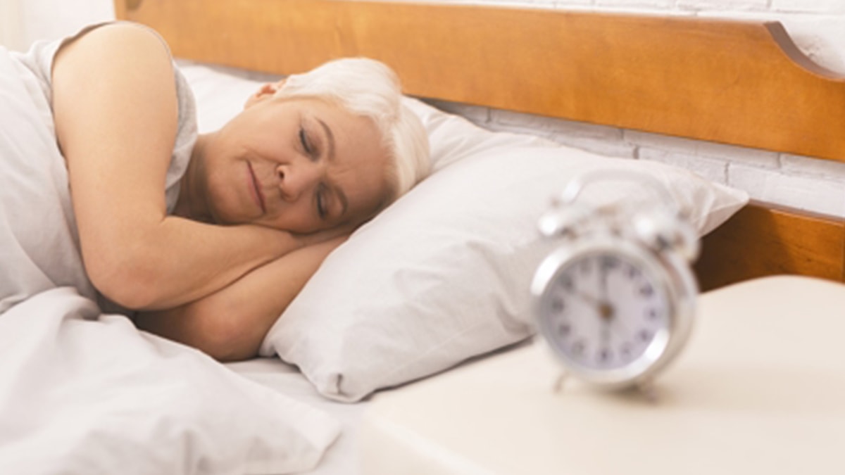 An old women sleeping on a mattress with an alarm clock kept beside her. 