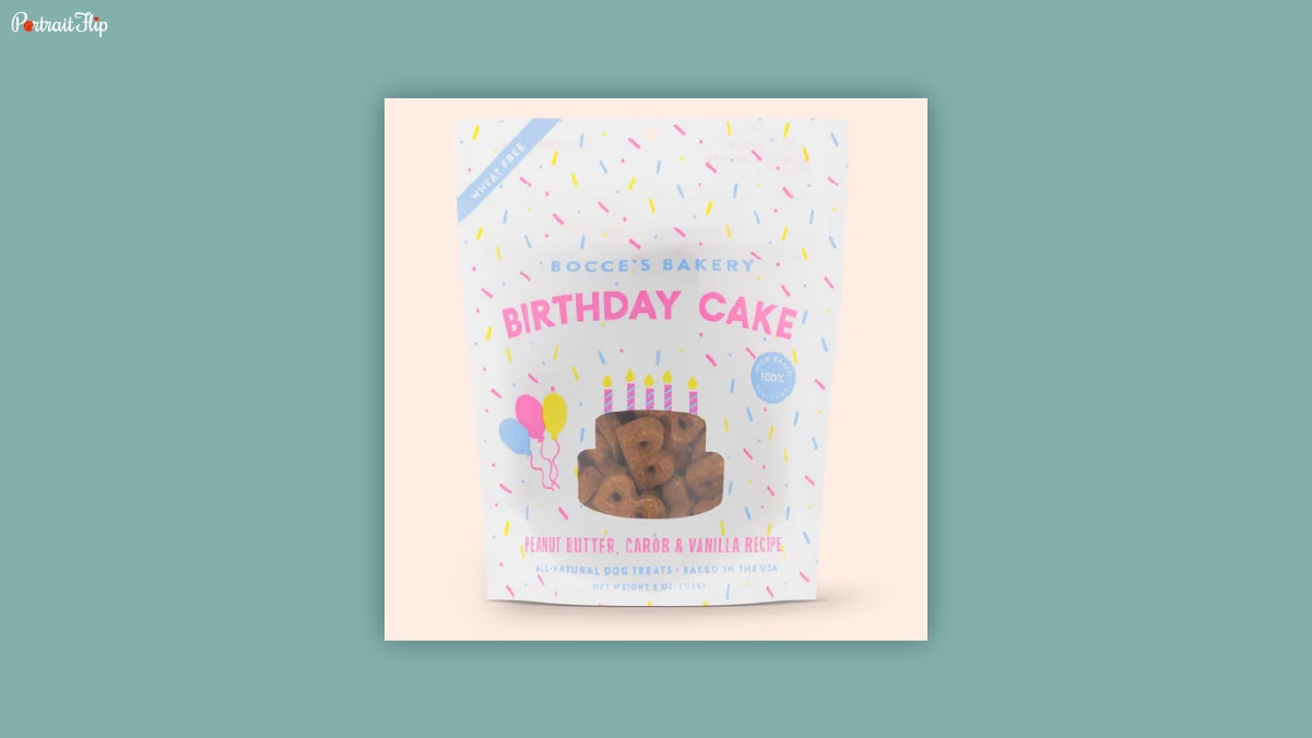 A white packet with birthday cake written on it in pink color kept on a light pink background as dog birthday gifts. 