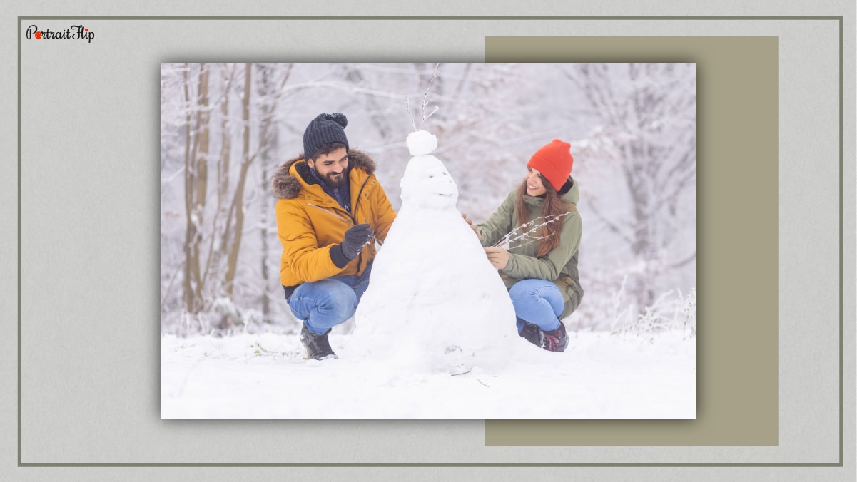 A couple building a snowman and both, the man and the woman are smiling. 