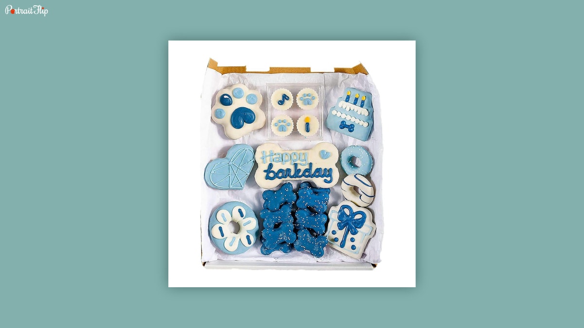 A pack of different shaped white and blue colored cookies for dogs on a white background as dog birthday gifts.