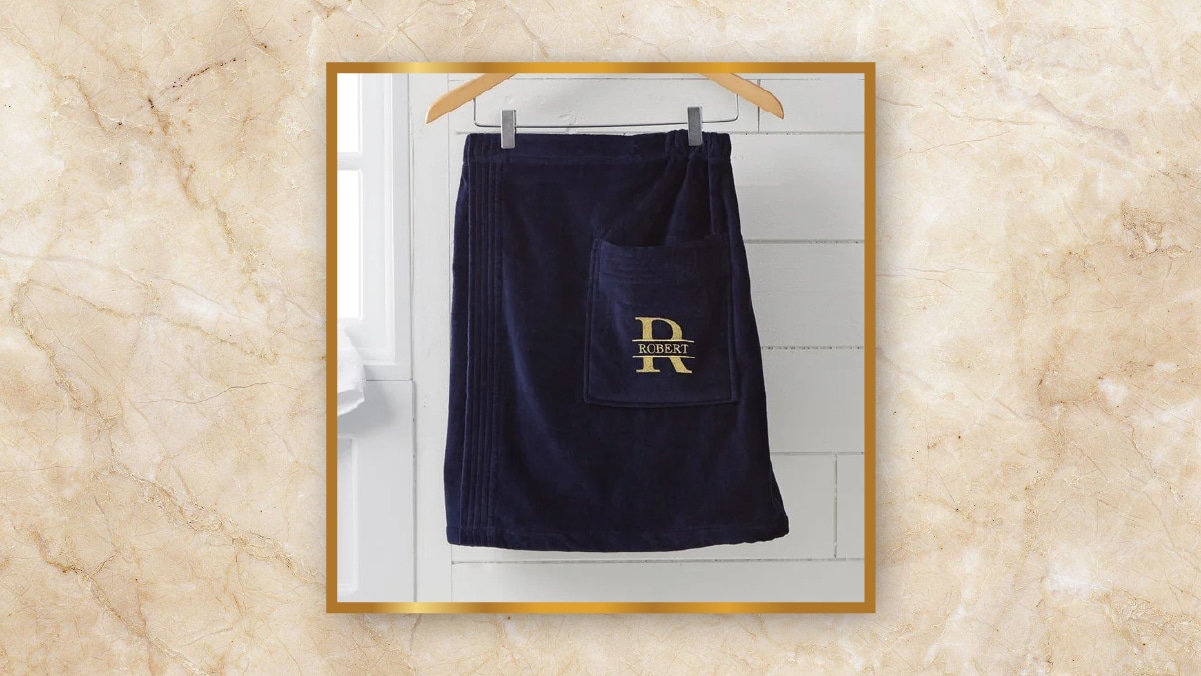 A dark blue colored towel hanging on a hanger with Robert embroidered on it with golden color on a white background. 
