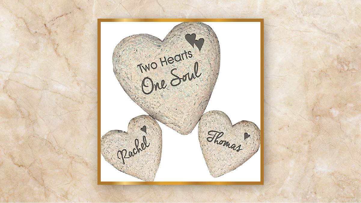 Three heart shaped garden stones with "Two heart one soul" and names written on them kept in a white background as personalized wedding gifts.