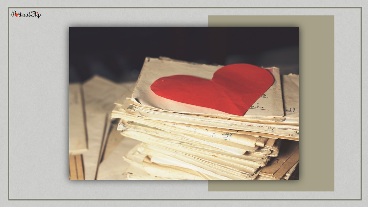 A pile of handwritten letters with a red paper heart on the top of the pile. 