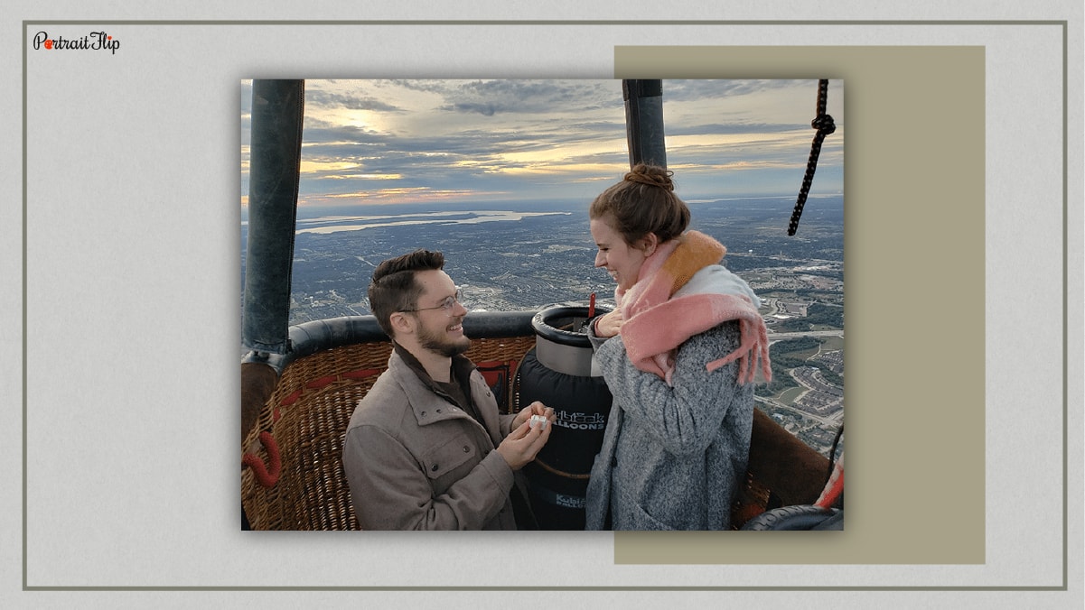 A man is on his knees proposing to his girlfriend on a hot air balloon. 