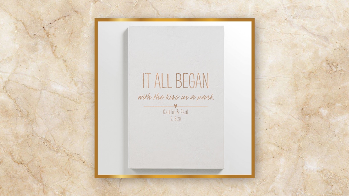 A white colored book with "IT ALL BEGAN" written on it in a golden frame kept in a white background. 