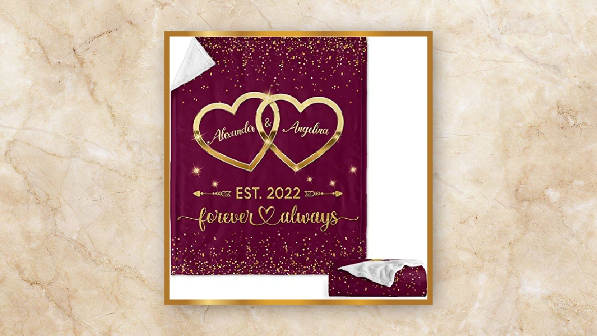 A maroon colored blanket with two hearts printed on it, kept in a white background as personalized wedding gift. 