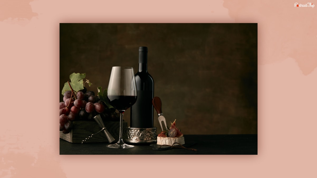 Bottle of wine placed beside a glass of wine, few grapes in a dark background.