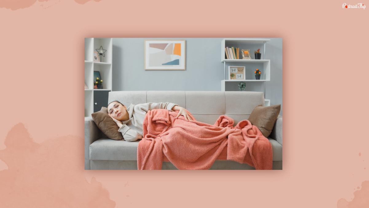 A woman sleeping on a couch half covered with throw blanket.