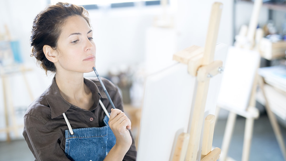 a beautiful girl is thinking and her paint brush is tilted and touched to the tip of the chin 
