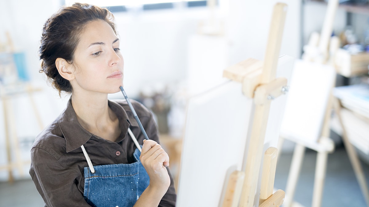 a beautiful girl is thinking and her paint brush is tilted and touched to the tip of the chin