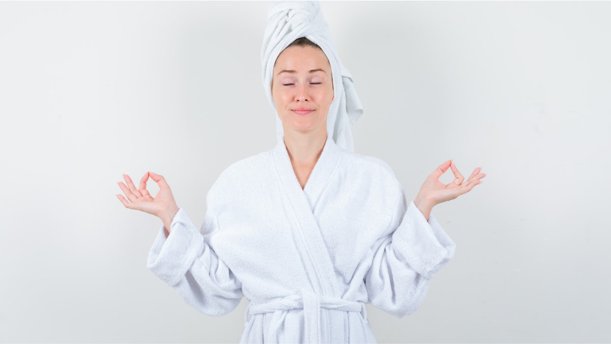 A girl in a bathrobe is smiling and meditating in a standing position.