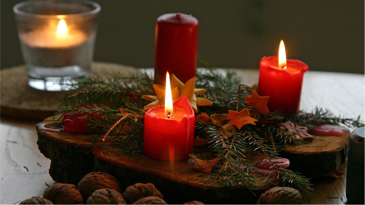 Three red colored Christmas candles are placed on the wooden surface with some leaves around them.