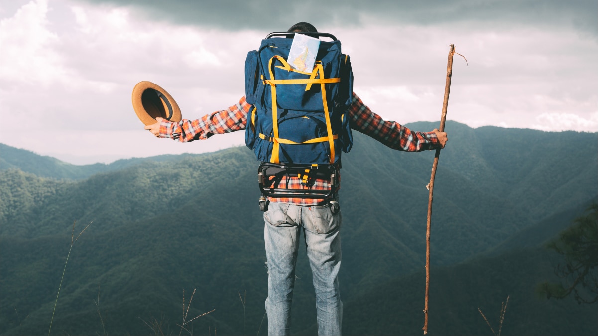 A man with his hiking backpack is seen in open hands on the mountain. 