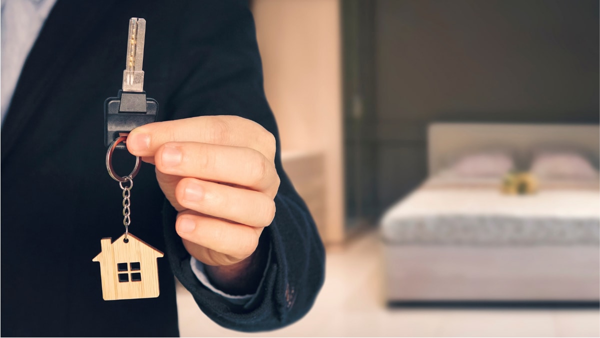 A man in a suit shows a key in a house-shaped keychain. 

