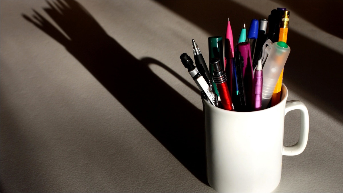 A white plain pen holder's shadow is being seen on the plain surface. 
