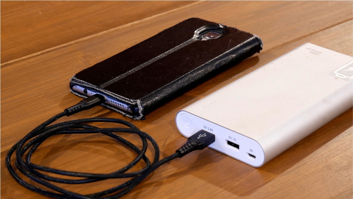 A portable charger is charging the mobile and both of them are placed on wooden surface.