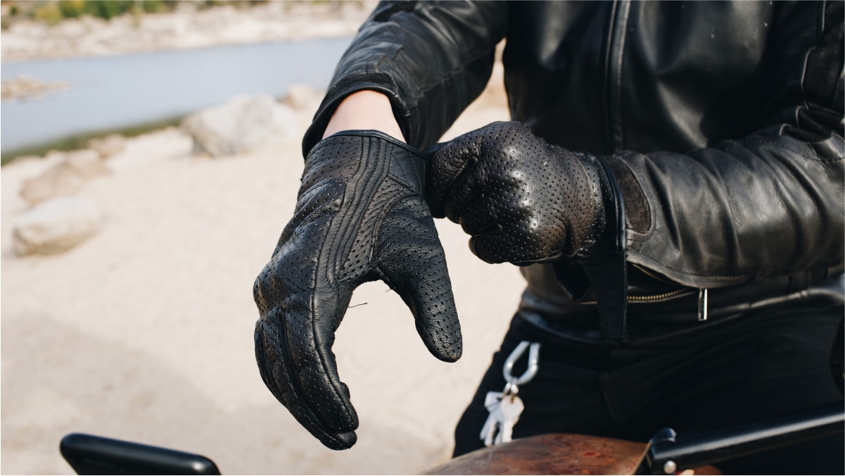 A man wearing his black rider gloves before turning on the vehicle. 