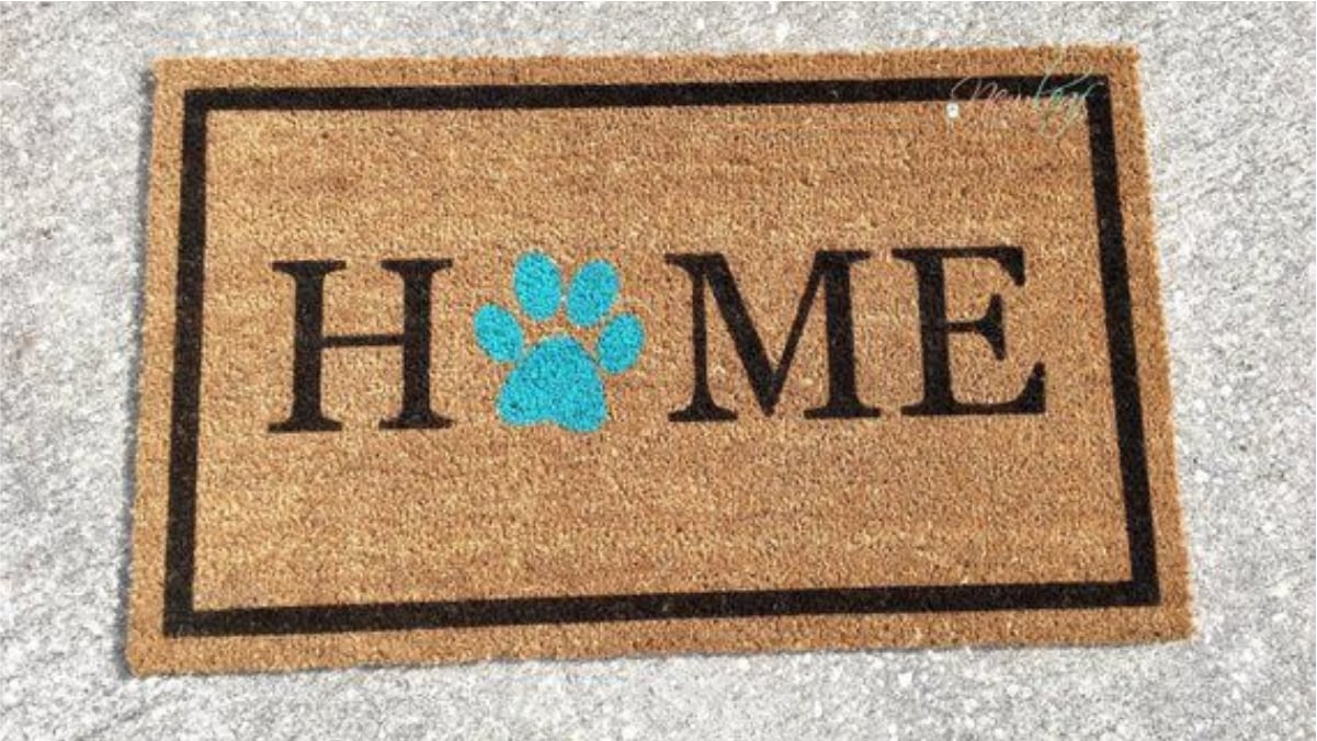 A brown colored welcome mat is placed on the grey surface. 