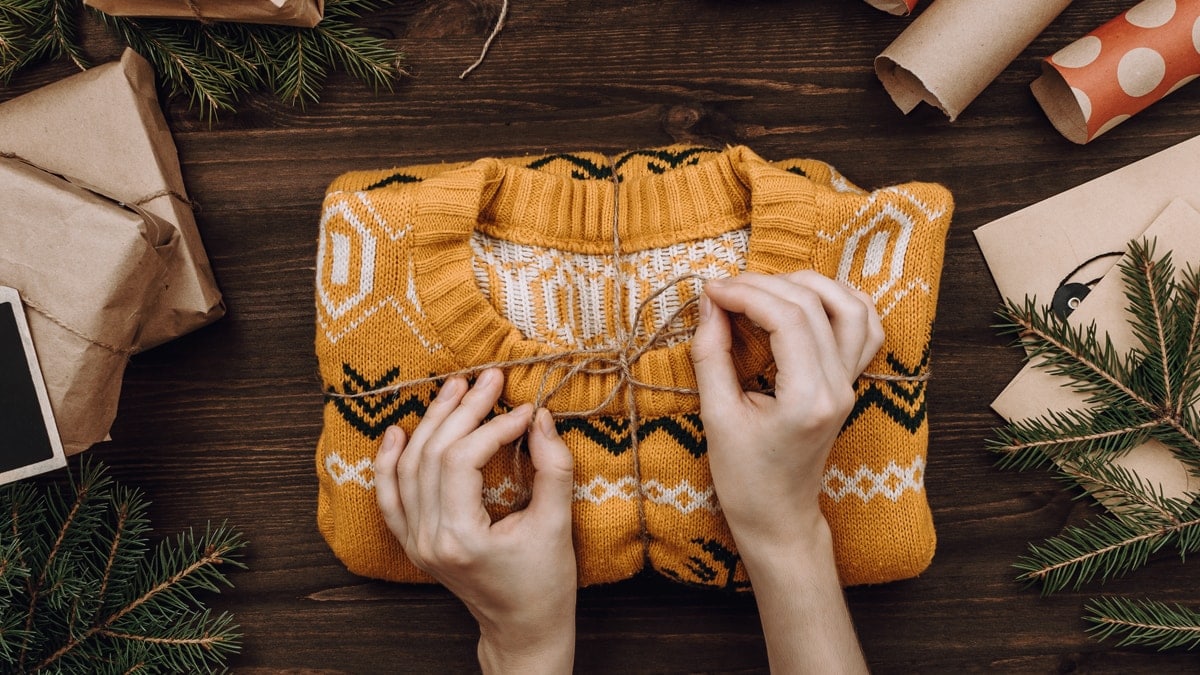 Woman's hands packing knitted sweater as present on dark wooden table