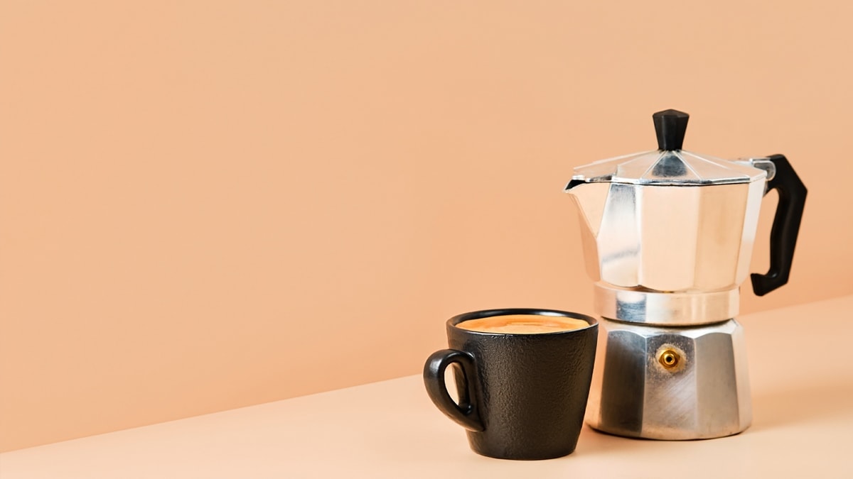 Cup with espresso coffee and Stovetop Espresso Maker on colored background 