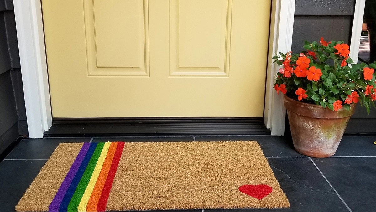 A doormat with rainbow print placed outside the door with a flower pot beside as a gifts for gay men.