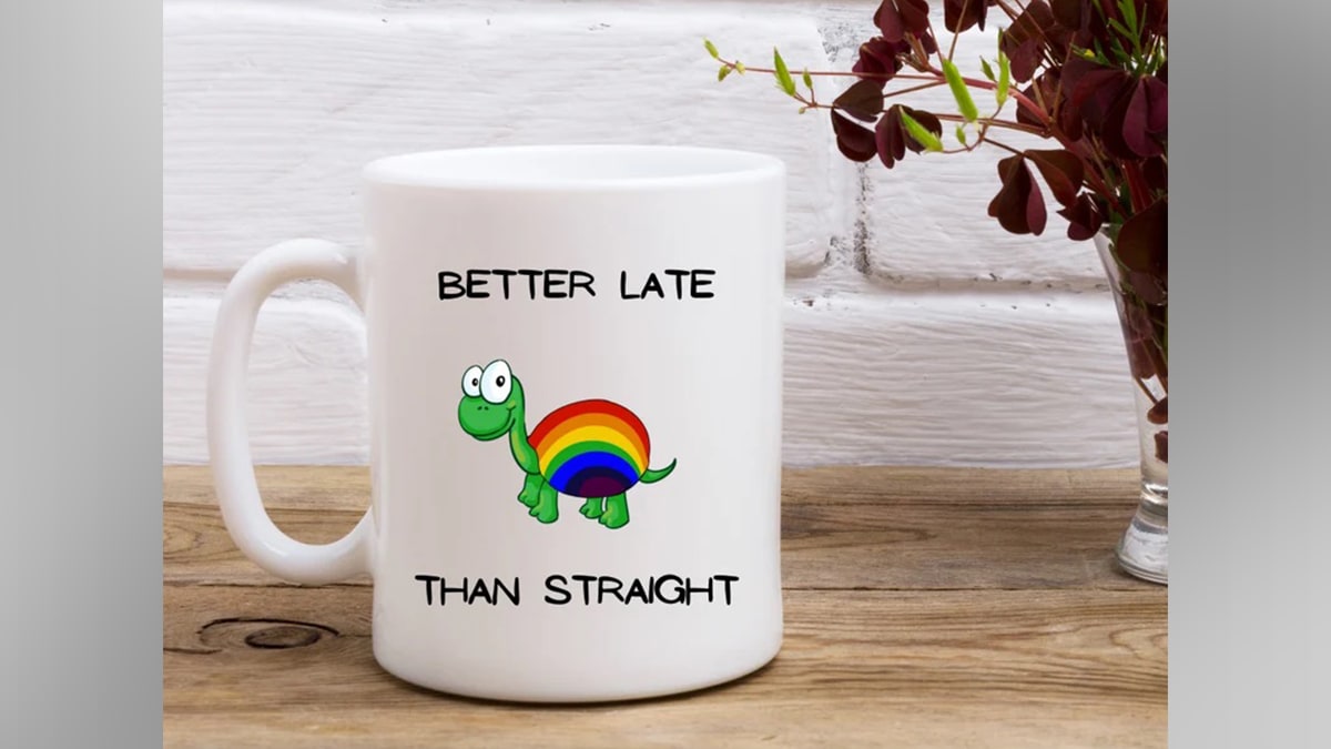 A mug with quote "Better late than straight" along with a small turtle indicating the pride symbol placed on a wooden table.