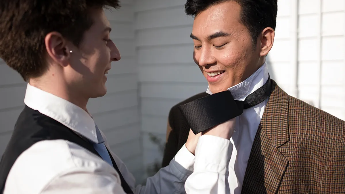 A gay man helping another man to wear a tie as a gifts for gay men.