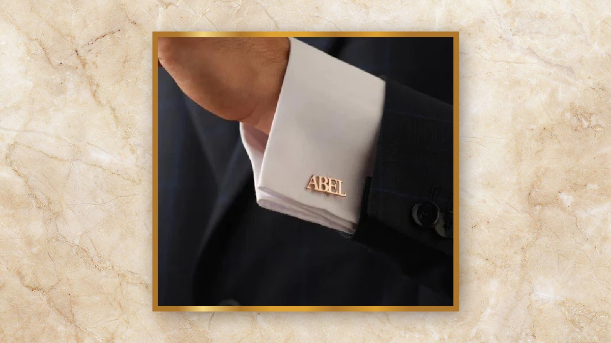 A white colored cuff with cufflinks saying "ABEL"  in a black blazer.