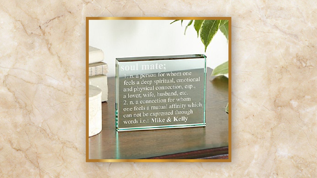 A transparent glass frame with soulmate written on it kept on a wooden table.  