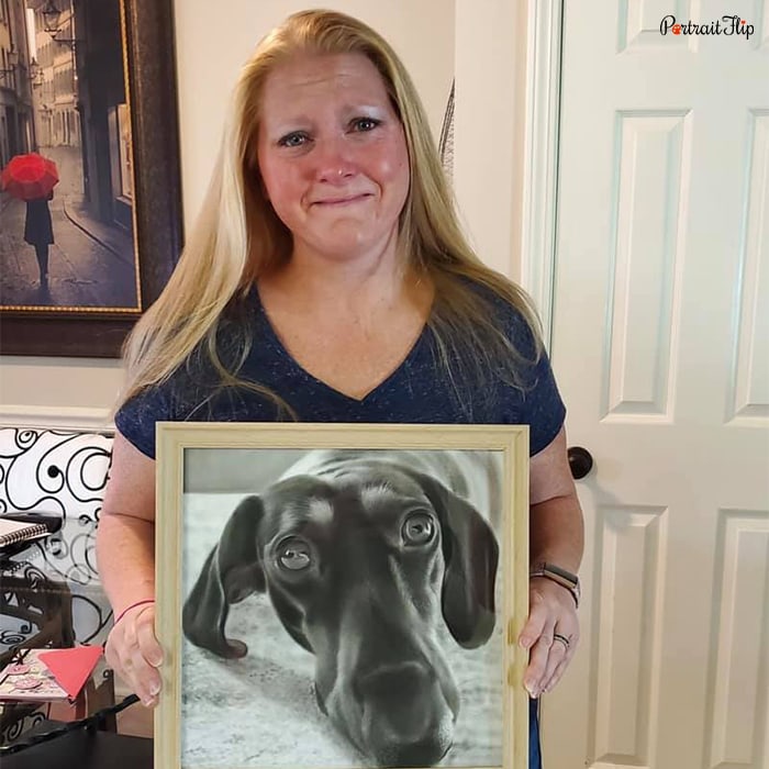 Picture of a woman holding pet portraits that portray her dog's face in black and white