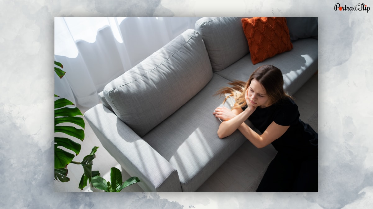 A woman sitter near couch with a sorrowful expression from a pet loss