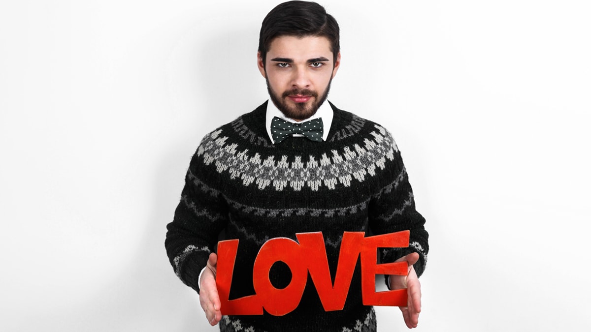 A gay man wearing a sweater as a gifts for gay men with a love cutout in his hand.