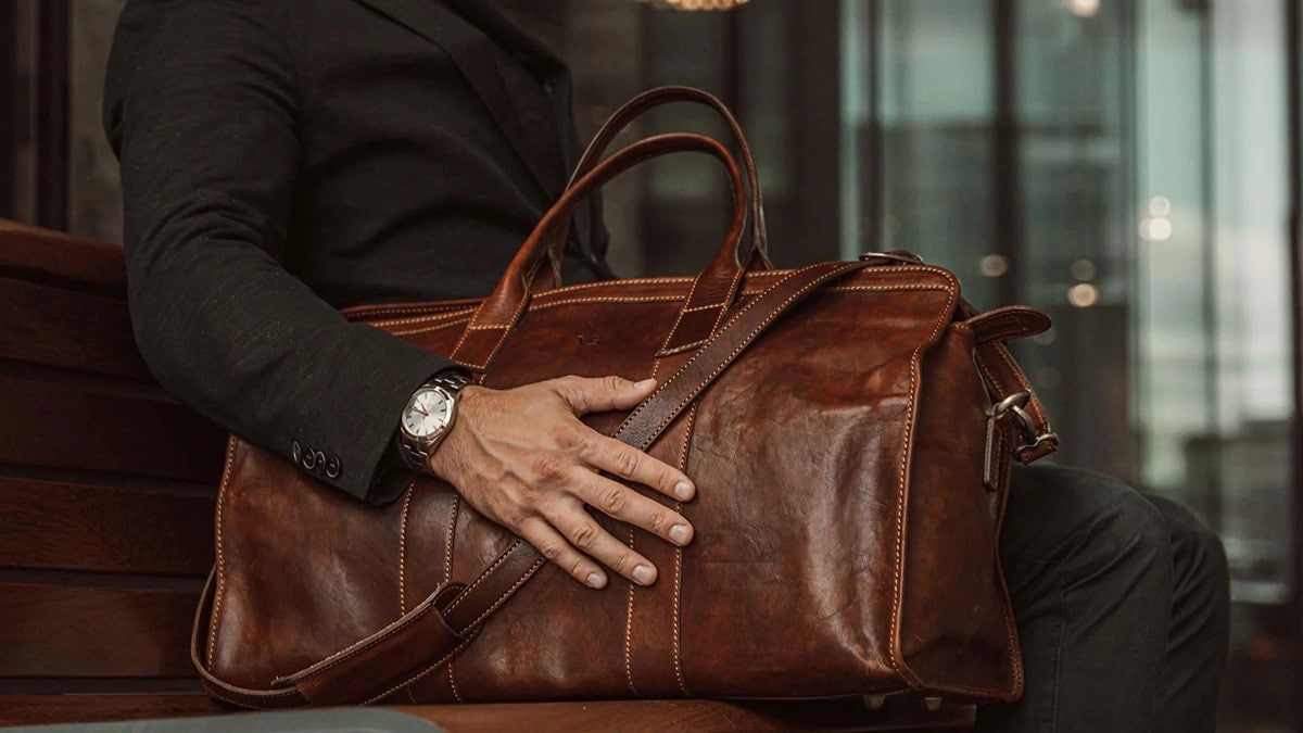 A man holding a custom travel leather bag in deep dark brown color 