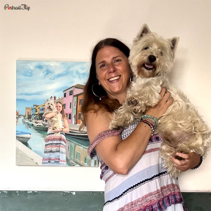 Picture of a woman holding her dog in her arms with same pose in portrait hanging on the wall
