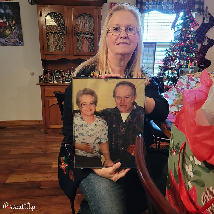 Picture of a woman holding Christmas portraits that include an old man and a woman