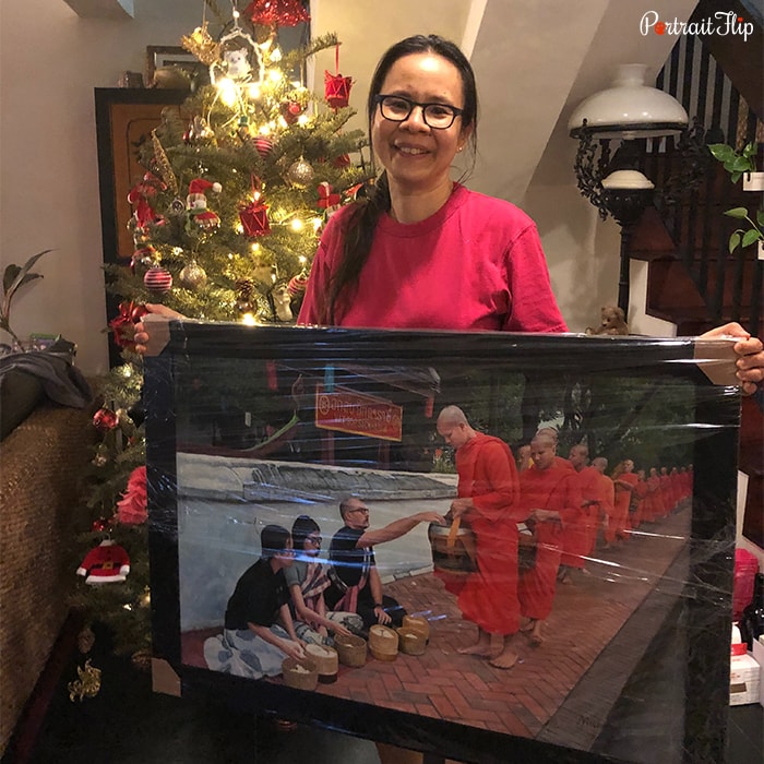 Picture of a woman holding Christmas portraits that include three people serving food to monks standing in queue