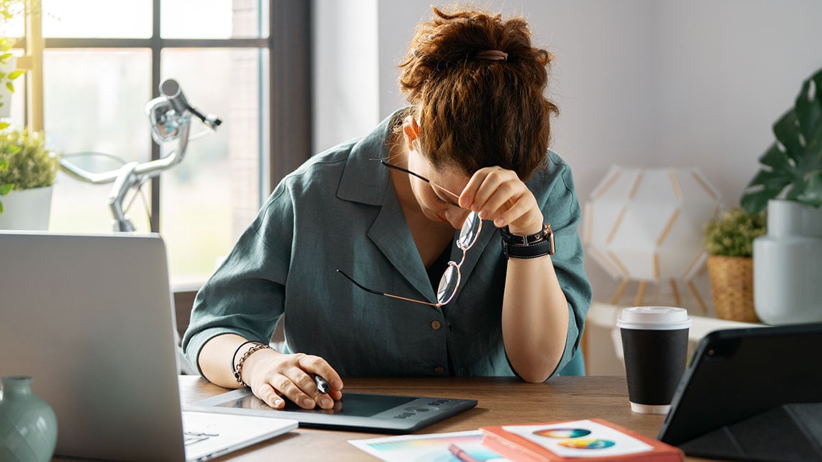 A woman with he hand on her head, showing tiredness and distress, while making digital art.