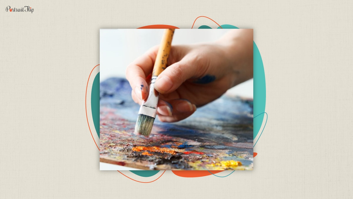 An artist's hand mixing paint with brush