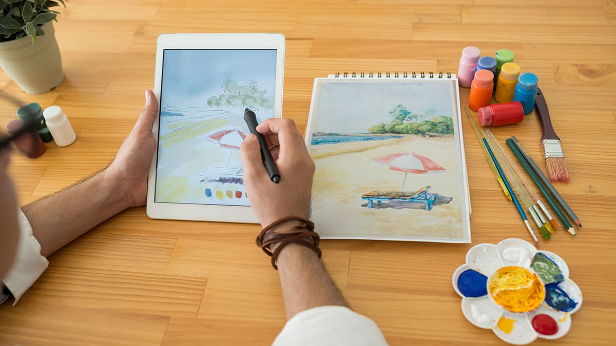 a man recreating a replica of a water color art on paper on his digital tab. 