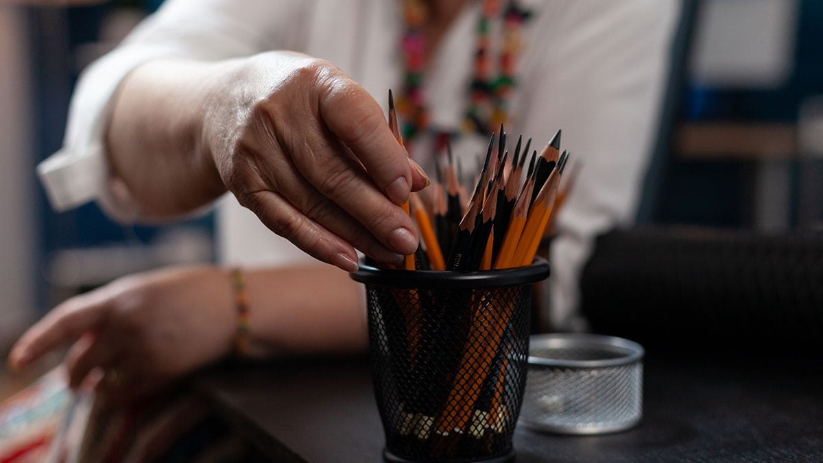 a older woman's hand reaching out for pencils. 