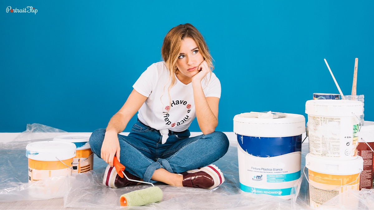 A woman sitting with paints around her in a thinking position