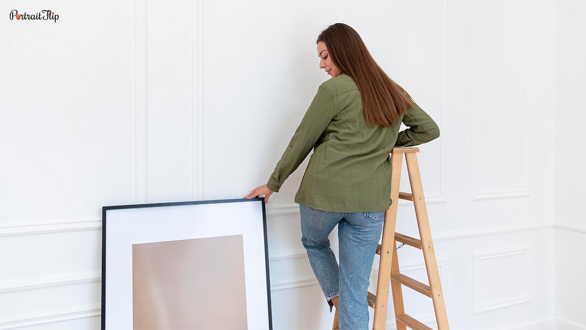 Woman trying to mount a frame on wall